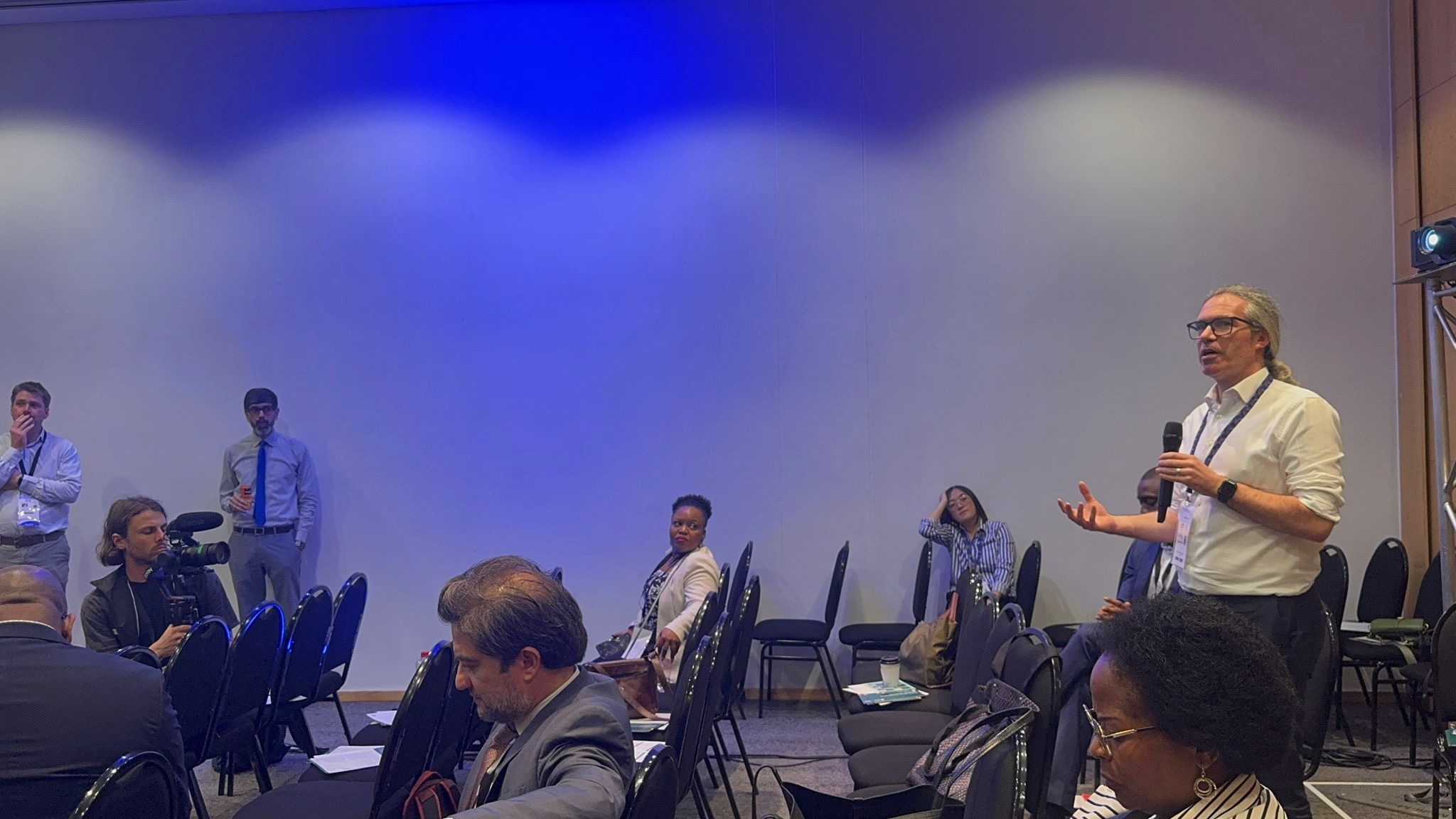 Picture of room at DPI summit with James holding the microphone